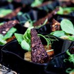 Close-up of gourmet appetizer in elegant black dishes with herbs and crisps, ideal for food presentations.